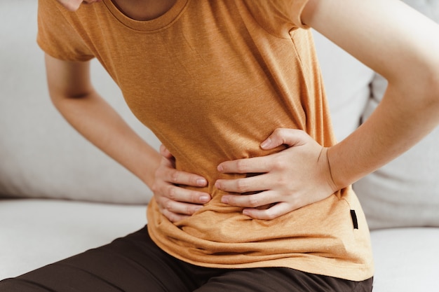 Junge Frau mit starken Bauchschmerzen, die zu Hause auf der Couch sitzt. Gastritis, Periode, Menstruation.