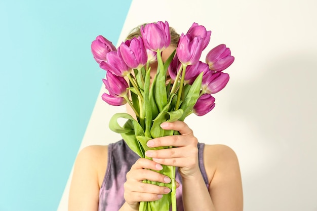 Junge Frau mit Strauß schöner lila Tulpen auf hellem Hintergrund