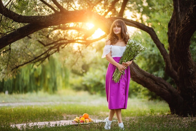 Junge Frau mit Strauß Wildblumen in den Händen vor dem Hintergrund des Sonnenuntergangs