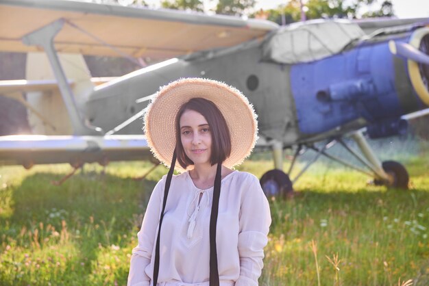 Junge Frau mit Strohhut steht vor einem Oldtimer-Flugzeug