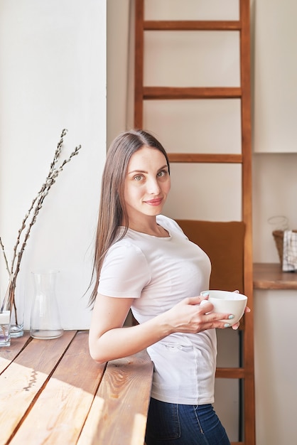 Junge Frau mit Tasse Kaffee oder Tee am Fenster im Café. Guten Morgen Konzept. Gemütliches Frühstück. Mädchen im Café.