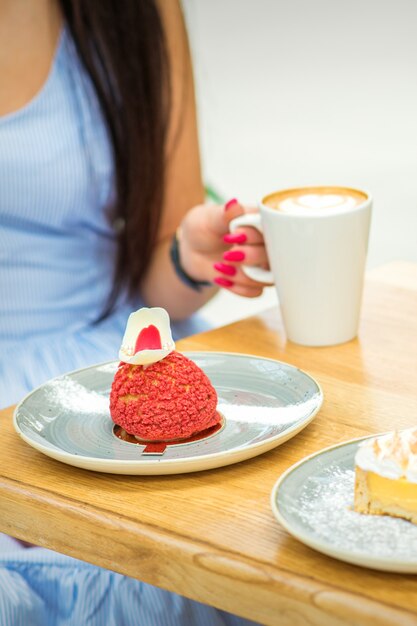 Junge Frau mit Tasse Kaffee und Stück Kuchen am Tisch in einem Café im Freien sitzen