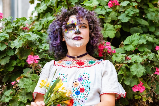 Junge Frau mit traditioneller folkloristischer Kleidung aus Mexiko und bemaltem Gesicht von La Calavera Catrina