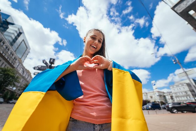 Junge Frau mit ukrainischer Flagge zeigt Herz mit den Händen