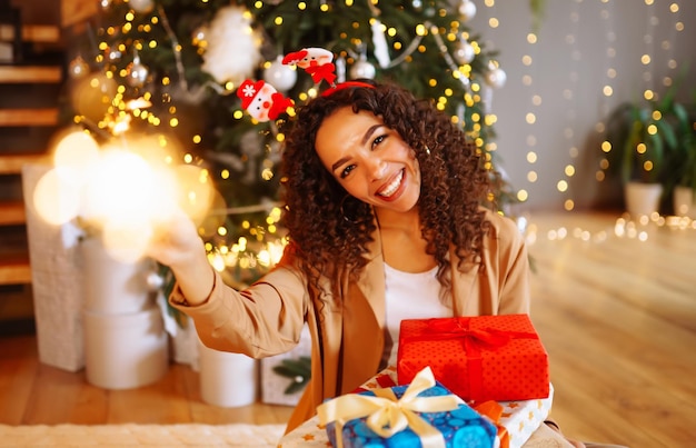 Junge Frau mit Weihnachtsgeschenken zu Hause in der Nähe von Weihnachtsbaum Winterurlaub Silvester