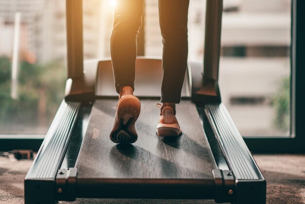 Foto junge frau mit weißen sportschuhen, die morgens mit sonnenlicht auf dem laufband geht, trainiert für kardiovaskuläre ausdauer und gute gesundheit im fitnesscenter