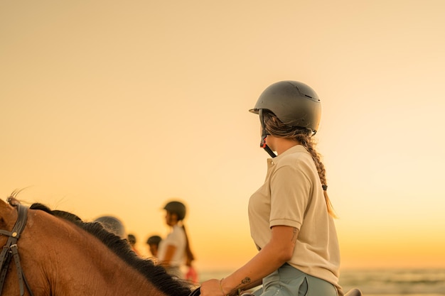 Junge Frau mit Zopf reitet zu Pferd und beobachtet ihre Gefährten