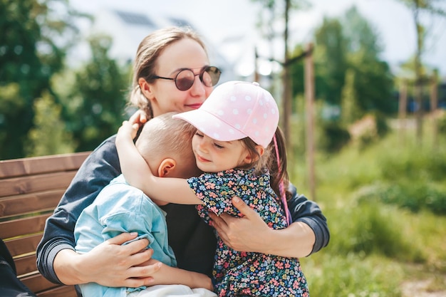 Junge Frau mit zwei Kindern - einem Jungen und einem Mädchen von 3-4 Jahren, die auf einer Parkbank sitzen. Glückliche Familie, die draußen Zeit miteinander verbringt.