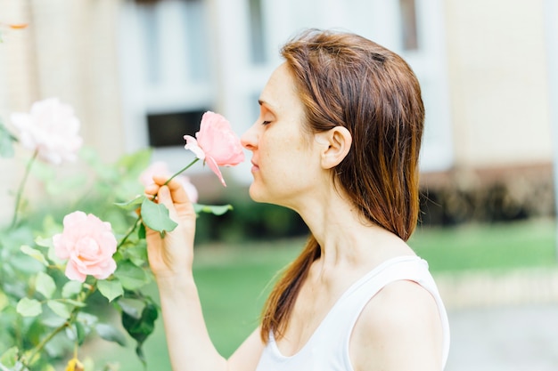 Junge Frau mittleren Alters im Park, die eine Rose hält, während sie daran riecht. Konzept mit der Natur verbinden