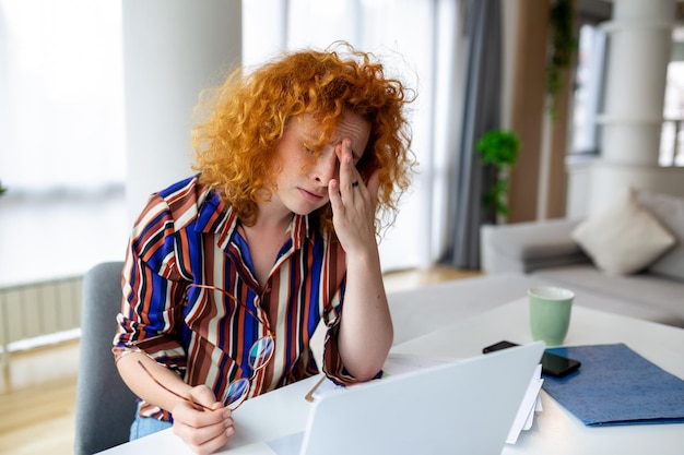 Junge Frau müde, erschöpft vom harten Studium, gelangweilt und frustriert, Kopf auf der Hand, heller Raum, große Fenster, zu Hause-Konzept, Stress-Konzept.