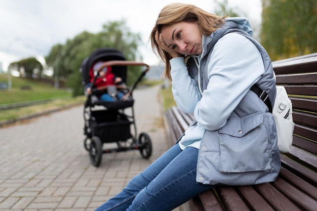 Junge Frau, Mutter einer postpartalen Depression, sitzt mit eingebauten Gefühlen im Park auf einer Bank daneben