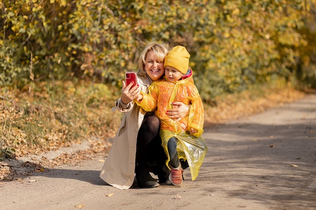 Junge Frau, Mutter eines kleinen Mädchens, benutzt Smartphone, um Videoanrufe mit ihren Verwandten zu tätigen oder macht Selfie mitten im Herbstpark