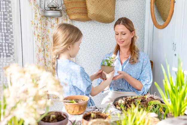 junge frau mutter und ihre kleine tochter in familienaussehen kleider pflanzen blumen auf der frühlingsterrasse in hause garten säulen wachsen landhaus veranda mutterschaft