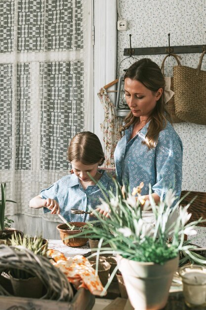 Foto junge frau mutter und ihre kleine tochter in familienaussehen kleider pflanzen blumen auf der frühlingsterrasse in hause garten säulen wachsen landhaus veranda mutterschaft