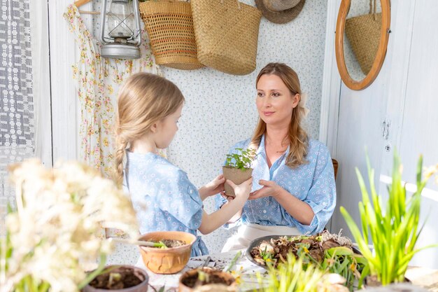 junge frau mutter und ihre kleine tochter in familienaussehen kleider pflanzen blumen auf der frühlingsterrasse in hause garten säulen wachsen landhaus veranda mutterschaft