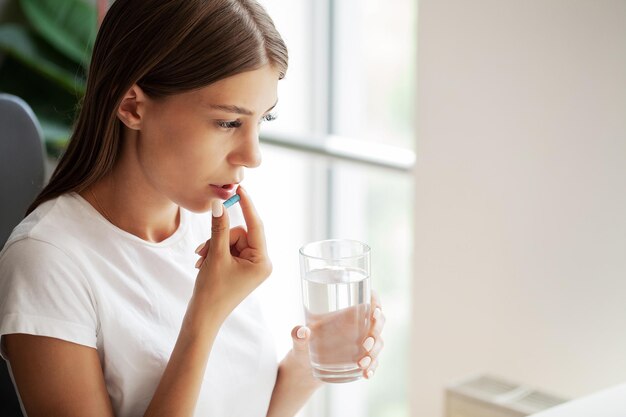 Junge Frau nimmt runde Pille mit Glas Wasser in die Hand