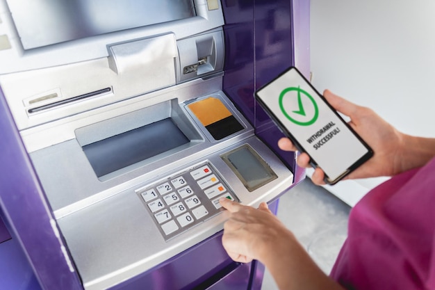 Junge Frau nutzt das Smartphone, um ohne Karte das Bargeld in der Nähe des Geldautomaten abzuheben