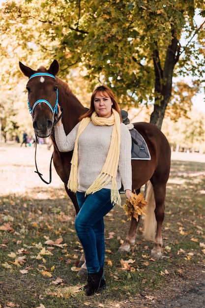 Junge Frau posiert in der Nähe von Pferd mit Herbstlaub