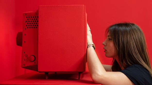 Junge Frau posiert in einem Studio mit roten Wänden und Möbeln Hält einen alten Vintage-Fernseher