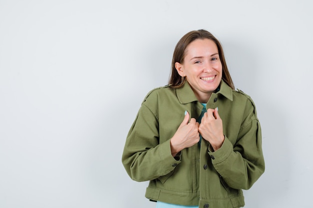 Junge Frau posiert mit den Händen über der Brust in der grünen Jacke und sieht beschämt aus, Vorderansicht.