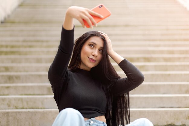 Junge Frau posiert mit ihrem Haar spielend lächelnd und macht Selfies mit ihrem Telefon