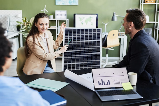 Junge frau präsentiert ihren kollegen während eines geschäftstreffens im büro ein solarpanel