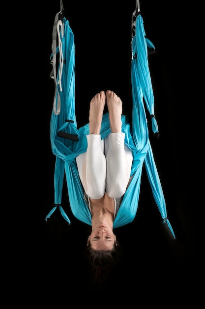 Junge Frau praktiziert Fliegen-Yoga auf Hängematten und hängt kopfüber Porträt des Fliegen-Yoga-Lehrers auf schwarzem Hintergrund