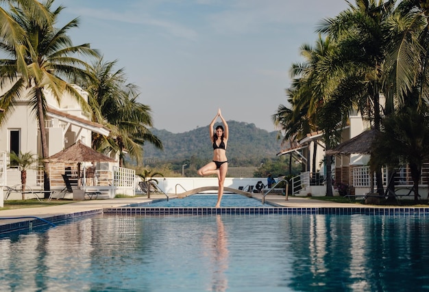 Junge Frau praktiziert Posen-Yoga am Swimmingpool und am Naturstrand bei Sonnenuntergang oder Sonnenaufgang Yoga und gesundes Konzept Yoga in Baumhaltung