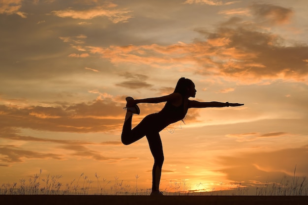 Junge Frau praktiziert Yoga am See bei Sonnenuntergang