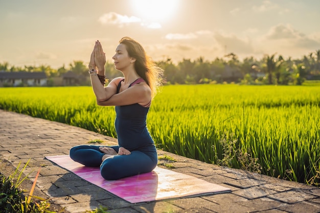 Junge Frau praktiziert Yoga im Freien in Reisfeldern am Morgen während des Wellness-Retreats in Bali