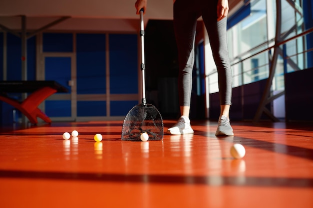 Junge Frau reinigt den Boden und pflückt Bälle nach dem Training oder Wettkampf im modernen Tischtennis-Sportverein