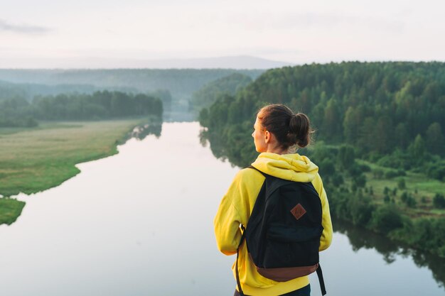 Junge Frau Reisende in gelbem Hoodie mit Rucksack, die den Sonnenaufgang auf der schönen Aussicht betrachtet Lokaler Tourismus-Wochenendausflug