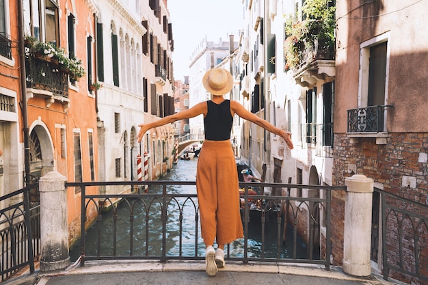 Junge Frau reist durch Italien. Urlaub in Europa. Mädchen genießen schöne Aussicht in Venedig. Weiblicher Tourist, der auf Straßen in Venezia geht. Modeblogger machen Foto auf der malerischen Brücke des Canal Grande.