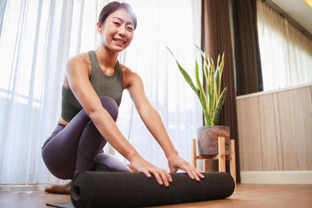 Junge Frau rollt schwarze Yogamatte aus, um zu Hause Yoga zu spielen, um sich von Covid19 unter Quarantäne zu stellen Neues normales Lebensstilkonzept