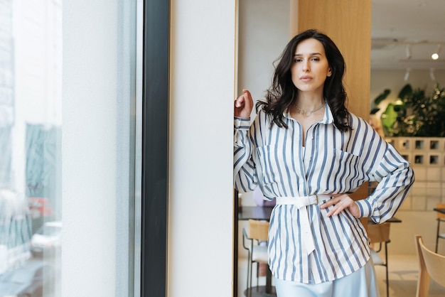 junge Frau ruht in einem schönen femininen blauen Kleid in einem hellen Raum am Fenster entspannen