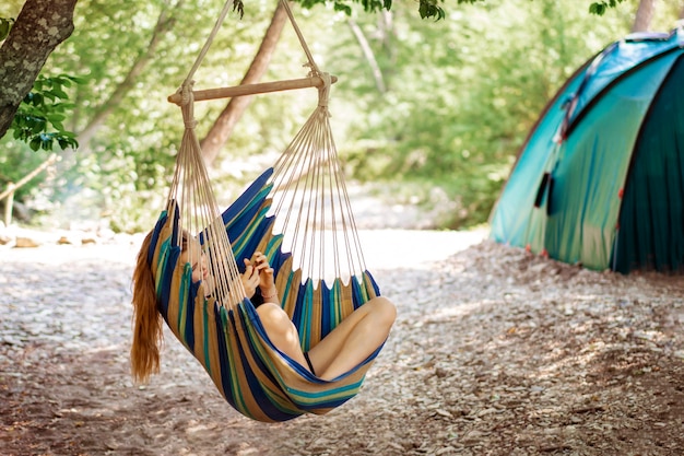 Junge Frau ruht in einer Hängematte im Wald beim Camping