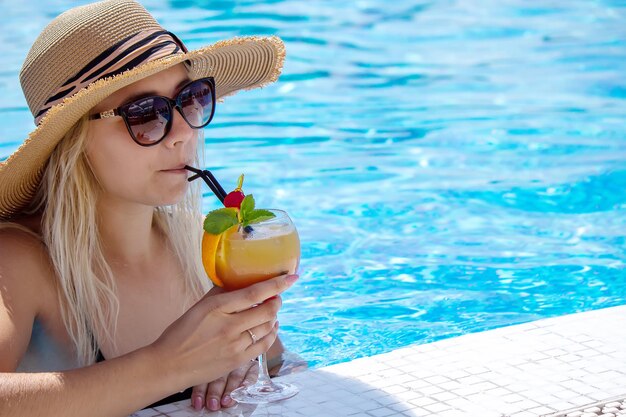 Junge Frau ruht sich im Pool aus. Trinkt einen Cocktail mit einer frisch gepressten Orange.