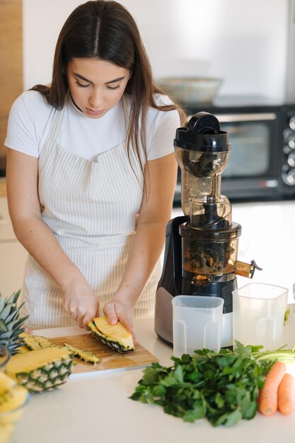 Junge Frau schält Ananas auf einem Holztisch und bereitet Früchte für hausgemachten Saft, ein veganes Getränk, vor