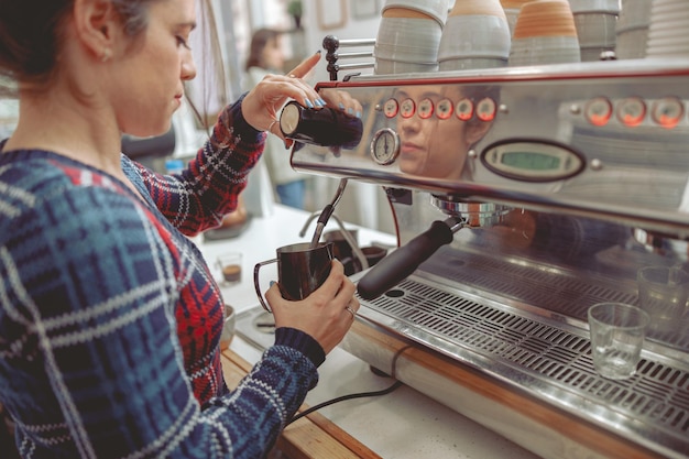 Junge Frau schäumt Milch für Latte in der Kaffeemaschine auf