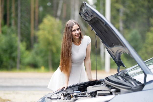 Junge Frau schaut unter die Motorhaube seines Autos, das kaputt gegangen ist