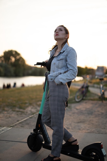 Junge Frau schaut weg, während sie auf einem Schubscooter gegen den Himmel steht