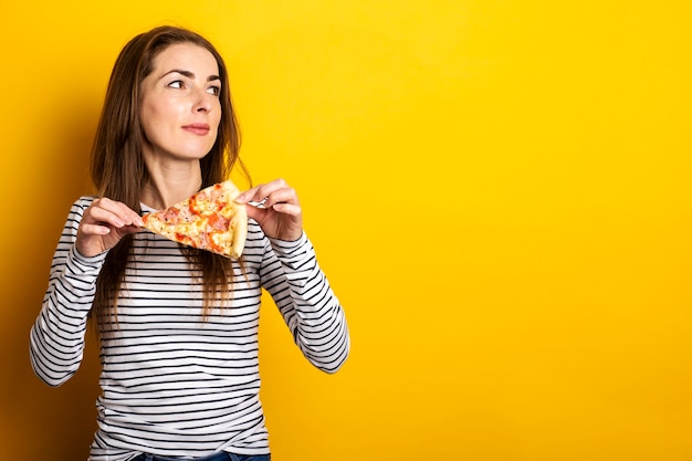 Junge Frau schaut zur Seite und hält ein Stück heiße frische Pizza auf einem gelben