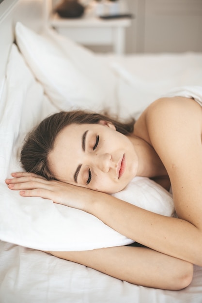 Junge Frau schläft friedlich im Schlafzimmer mit weißen frischen Laken, Augen geschlossen.