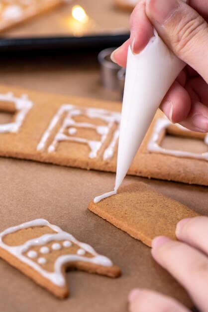 Junge Frau schmückt Weihnachten Lebkuchenhaus Kekse Keks zu Hause mit Zuckerguss in Spritzbeutel Nahaufnahme Lebensstil