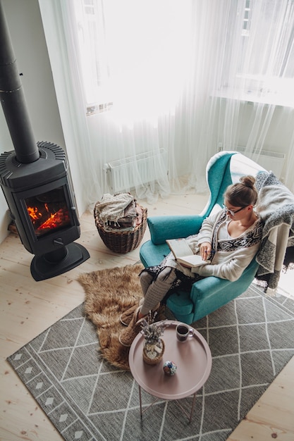 Junge Frau schreibt im Notizbuch, das im Sessel am Kamin sitzt