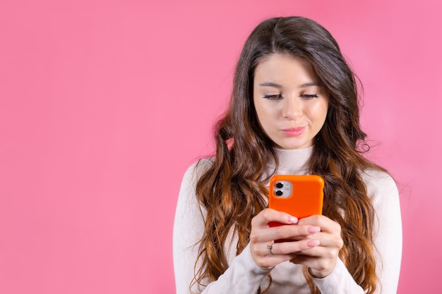 Junge Frau schreibt jemandem unglücklich eine Nachricht mit einem Smartphone auf dem rosa Hintergrund