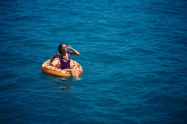 Junge Frau schwimmt auf einem aufblasbaren großen Donut im transparenten türkisfarbenen Meer Blick auf eine schlanke Dame, die sich im Urlaub in der Türkei Ägypten im Mittelmeer entspannt