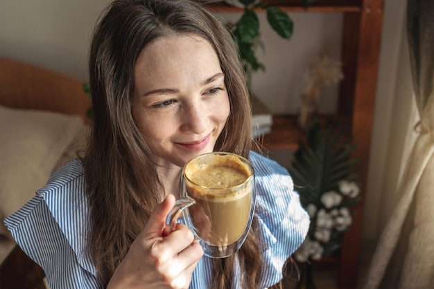 Junge Frau sitzt am Fenster und trinkt Kaffee und genießt einen sonnigen Morgen Konzept eines angenehmen Zeitvertreibs, gute Laune, Harmonie und Glück in kleinen Dingen