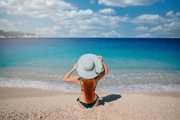 Junge Frau sitzt am Strand mit blauem Hut