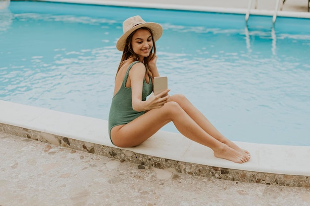 Junge Frau sitzt am Swimmingpool und macht Selfie-Foto mit Handy im Hinterhof des Hauses